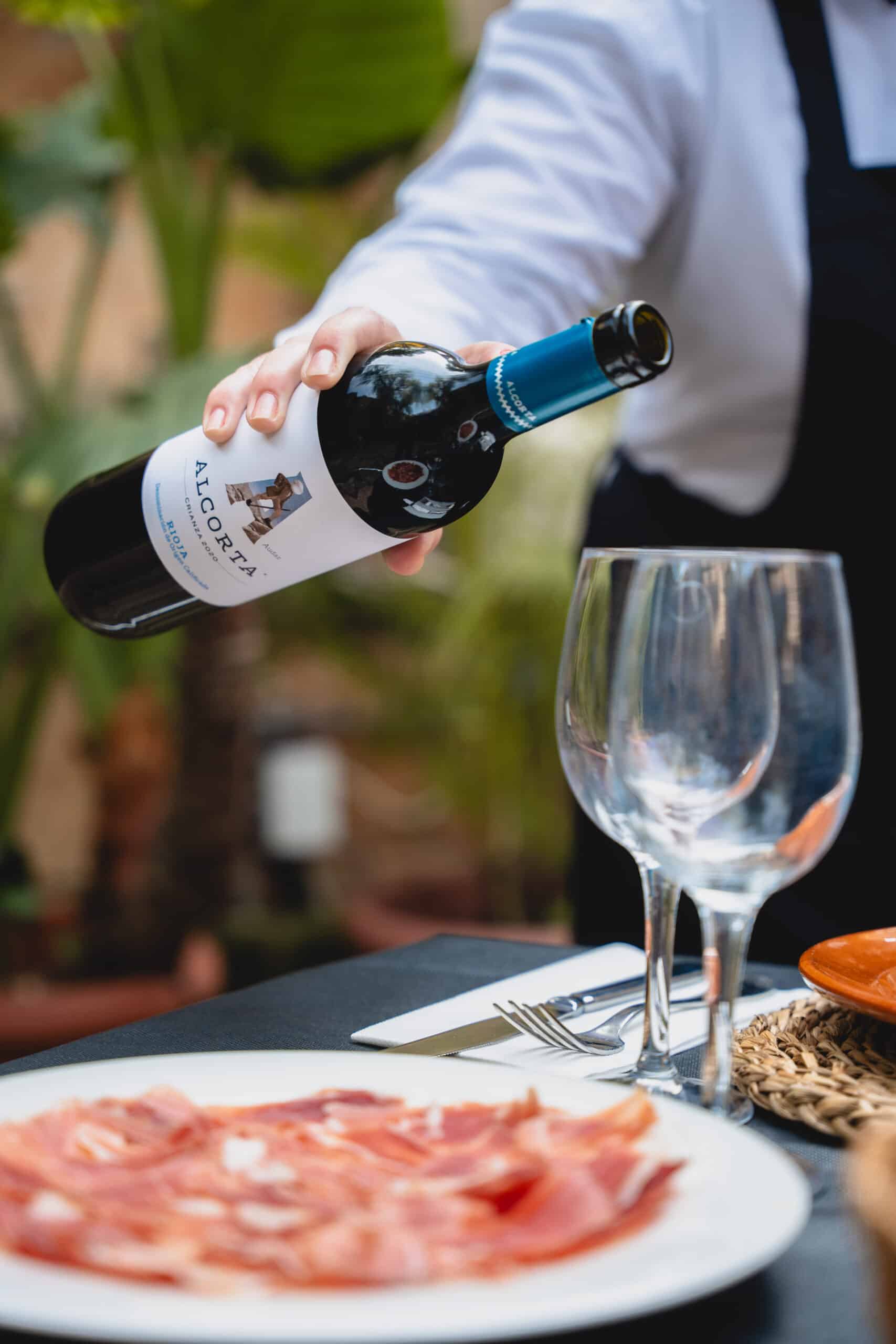 Botella de vino alcorta que se está sirviendo en una copa por un camarero del restaurante molí des comte